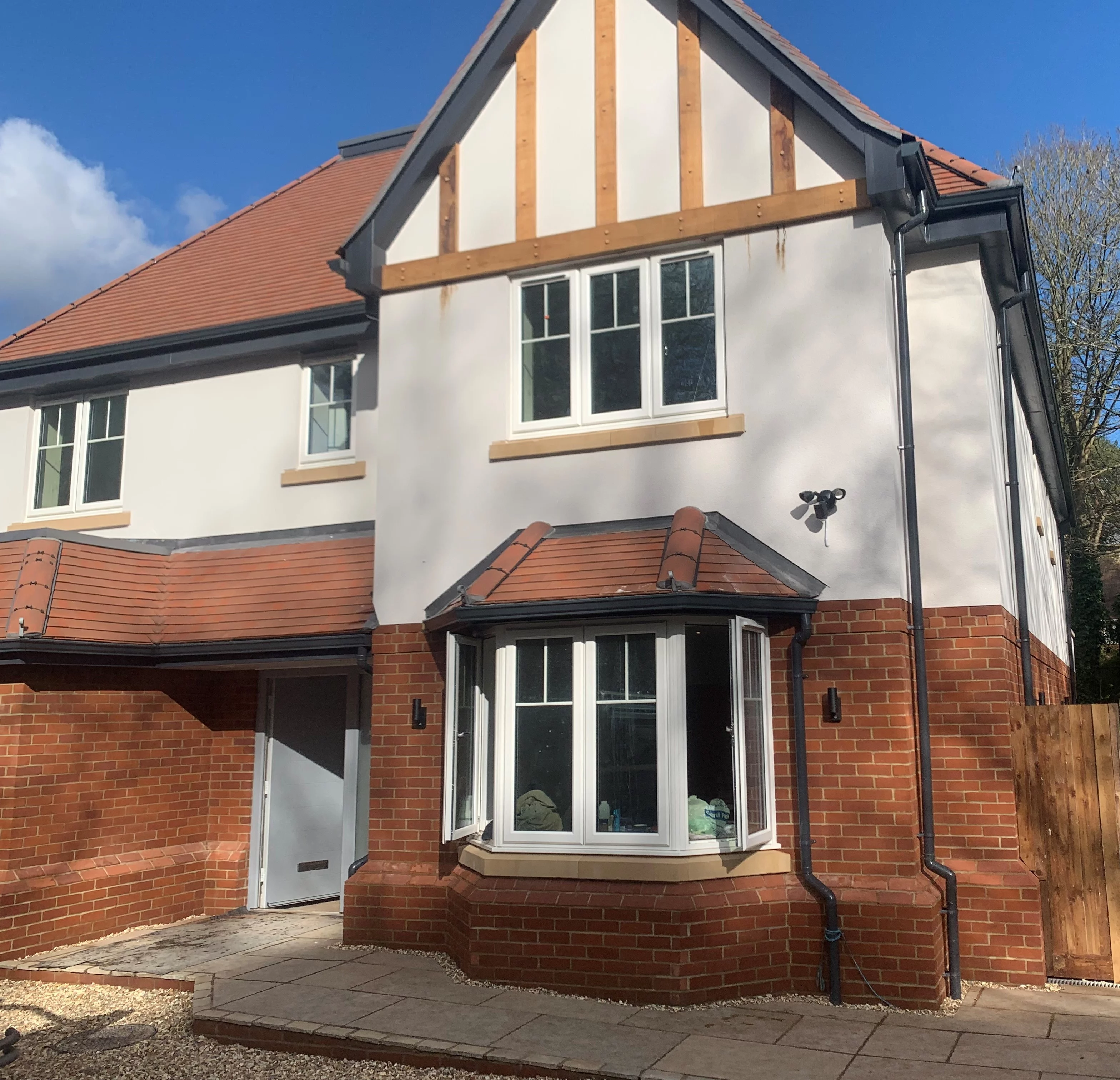 A modern two-story house with white walls, red brick accents, multiple windows, a bay window, and a tiled roof under a blue sky.