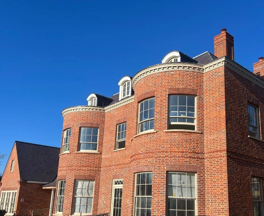 A red brick building with large rounded bay windows and dormer windows on the roof, under a clear blue sky.