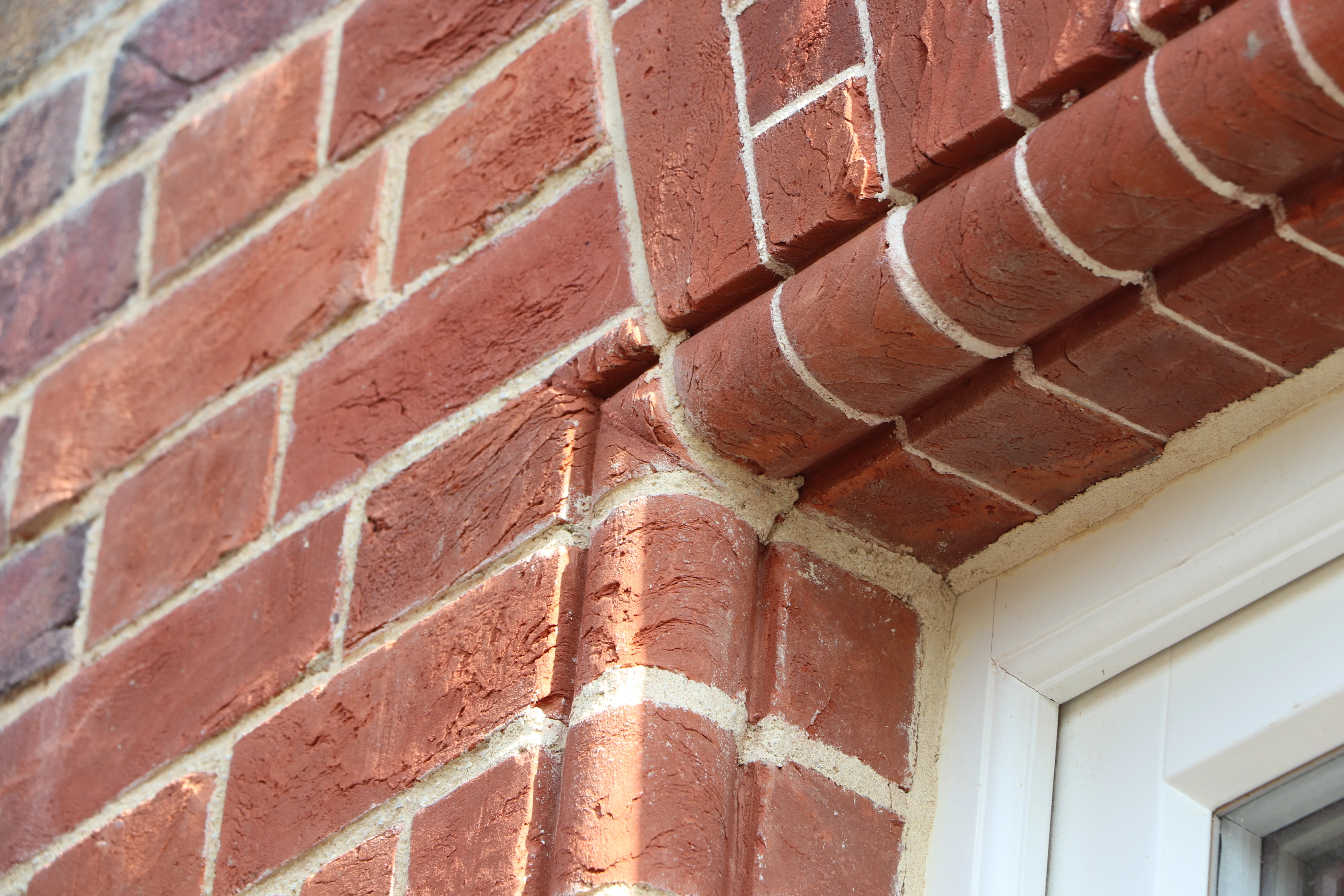 Close-up view of a red brick wall with white mortar, showing detailed brickwork around the edge of a window frame.