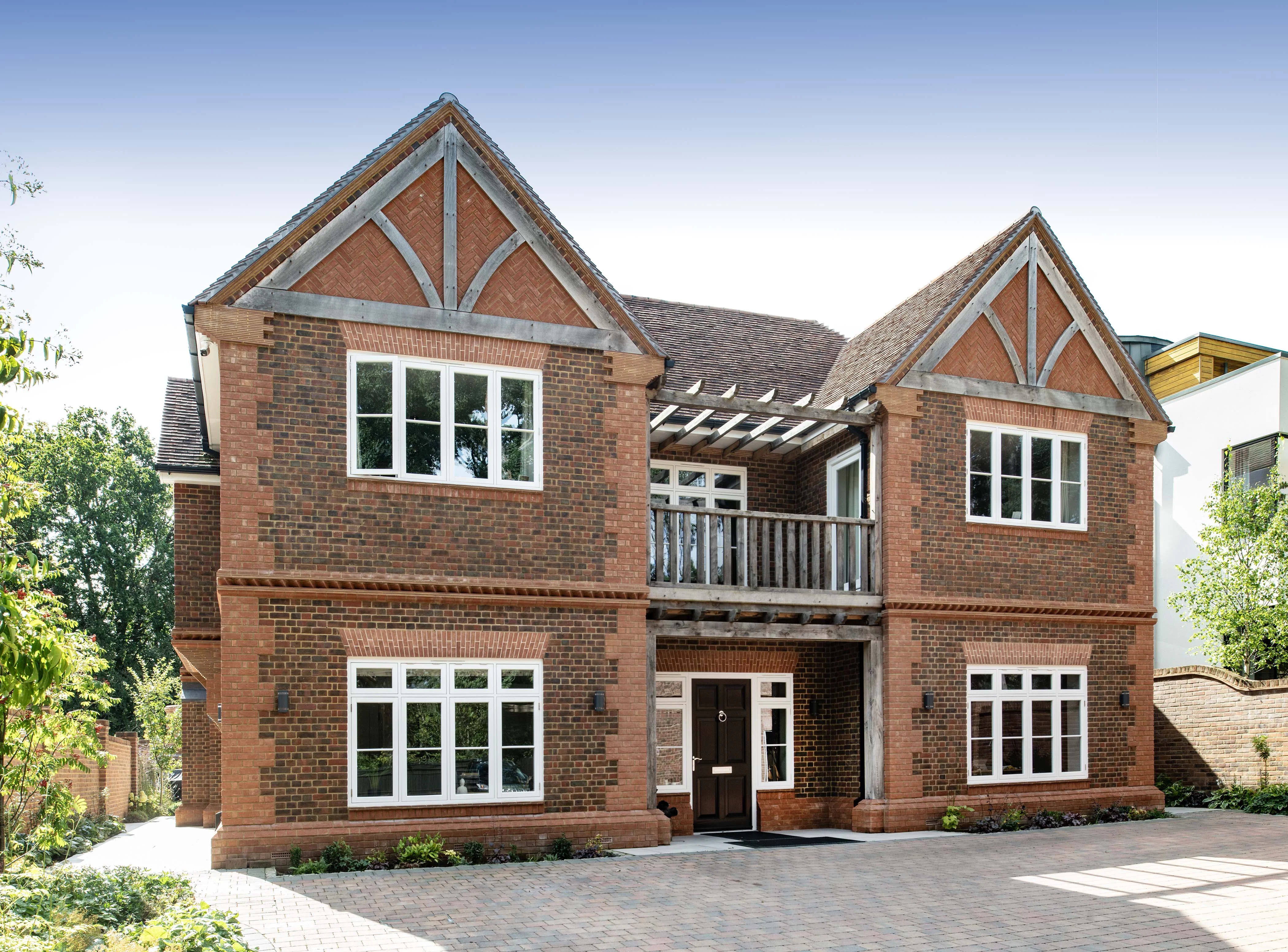 Two-story brick house with white-trimmed windows, gabled roofs, a small balcony above the front door, and a paved driveway in front.