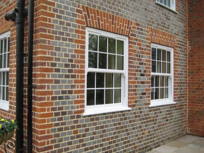 A close-up of a brick house exterior with two white-framed sash windows, each divided into six panes over six panes.