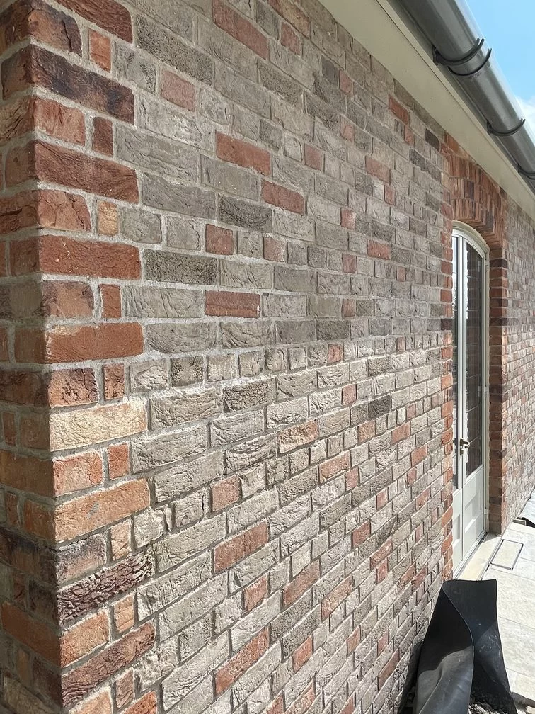 A brick wall with different toned brick colour and texture, next to a door, under a gutter.