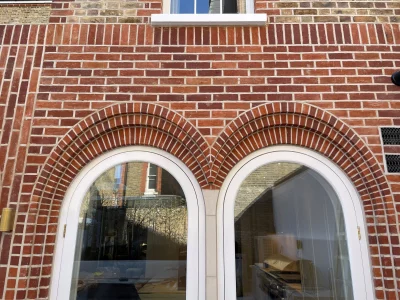 Two semi circular arched windows with two elliptical brick arches surrounding the top of them with a red brick wall