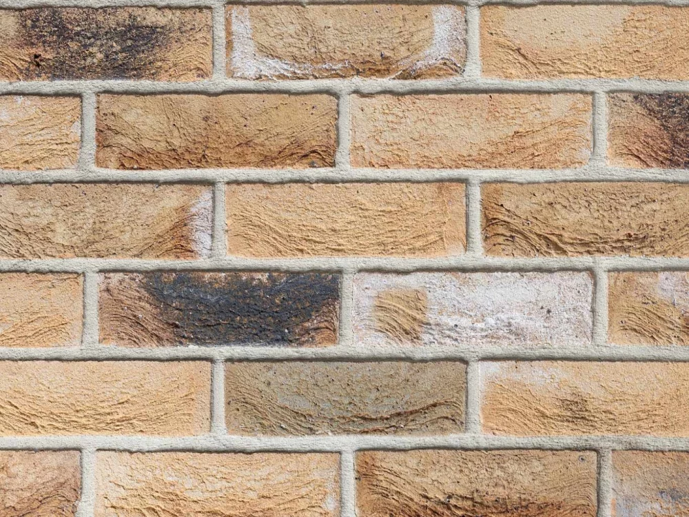 A wall with yellow and brown bricks laid in a stretcher pattern