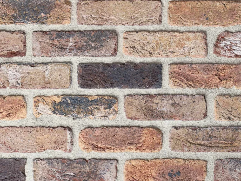 A close-up view of a Kempen Antique (C0186) brick wall featuring rough-textured, rectangular bricks in brown, red, and tan shades, separated by light grey mortar.