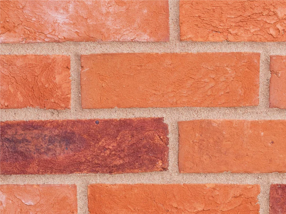 A red and orange brick wall with light mortar laid in a stretcher pattern