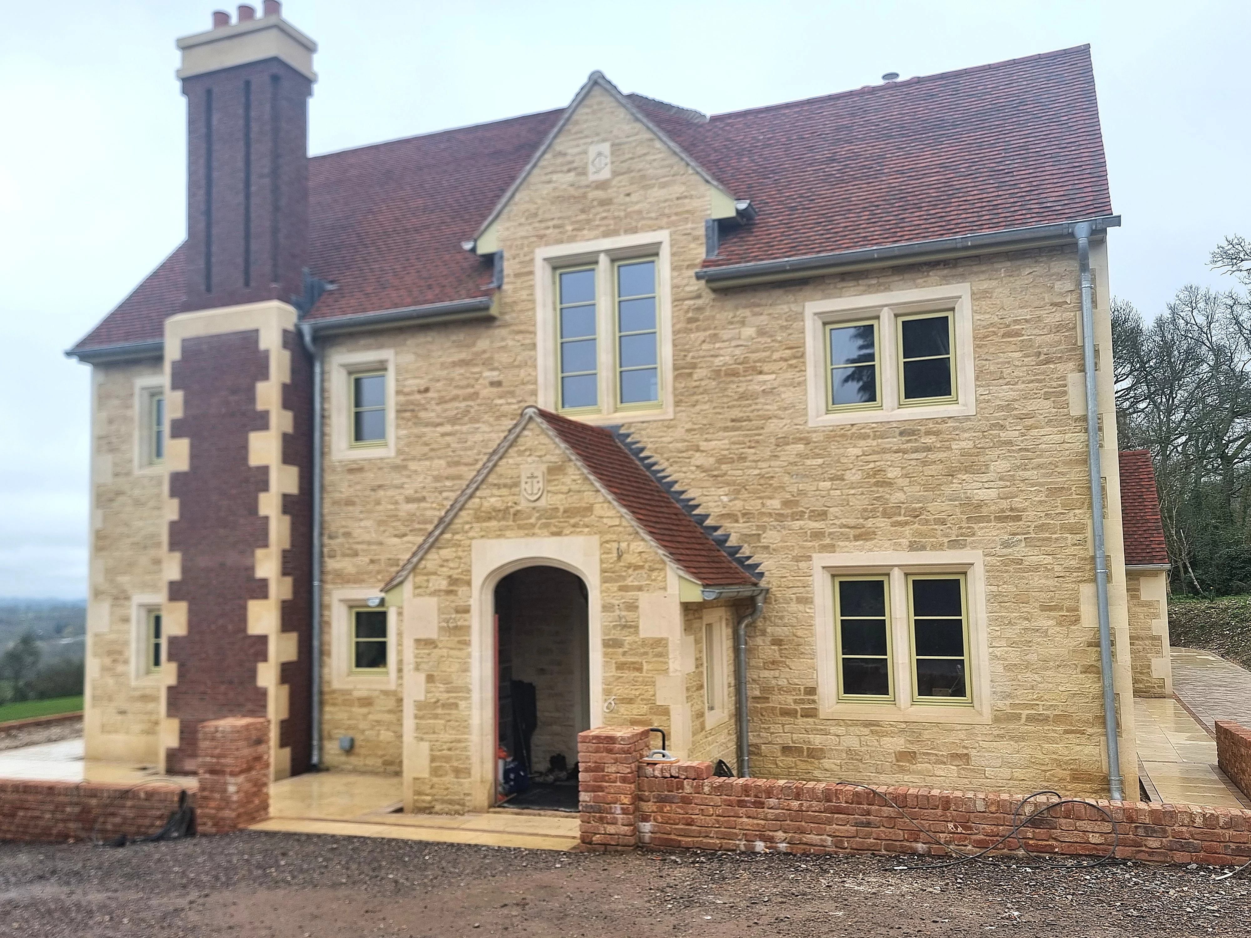 A traditional house with stone walling facade with a chimney breast cladded in brick to match the roof tiles. A stone porchway featuring stone surrounds and a stone plaque