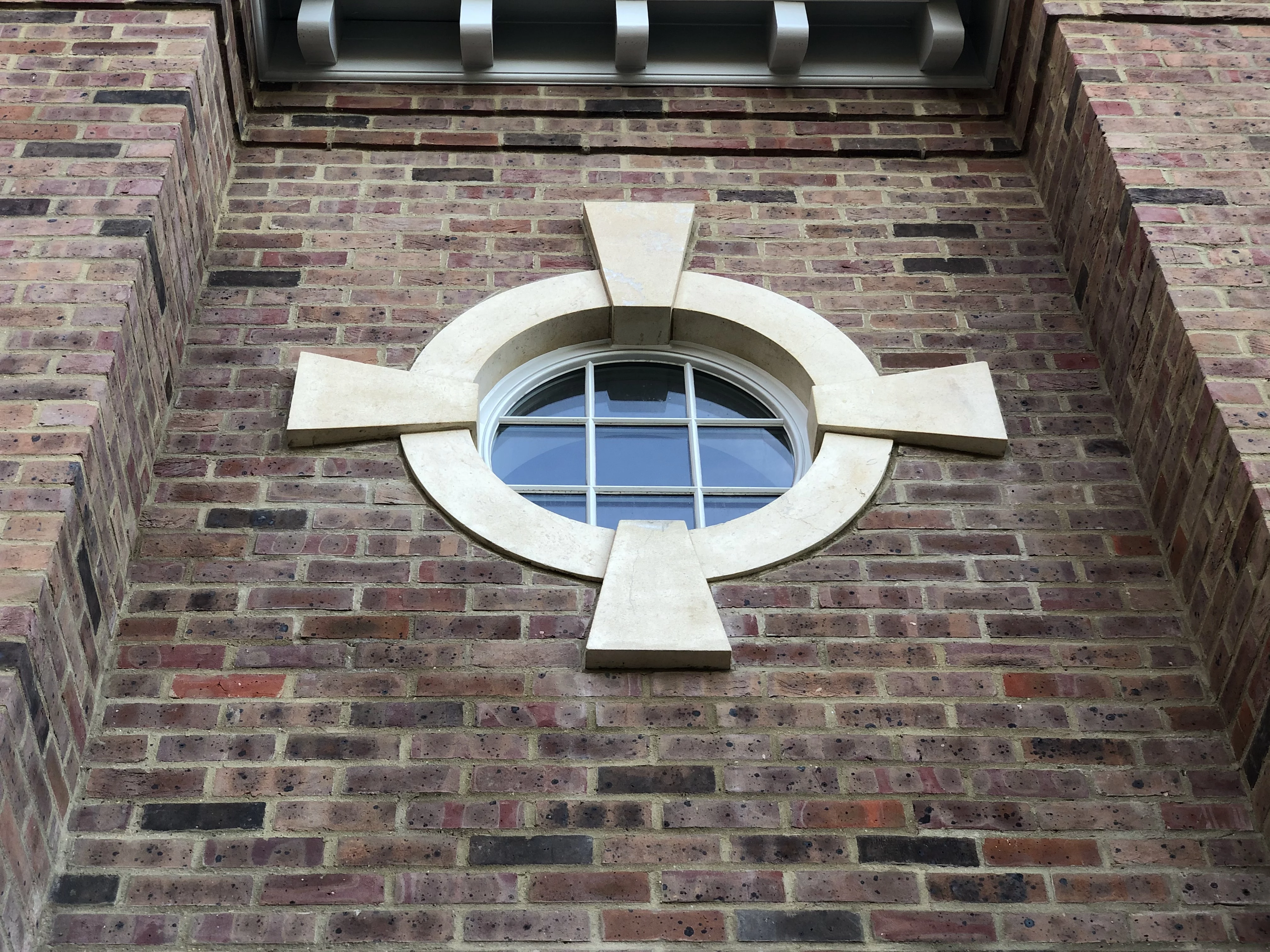 A stone bullseye arch surrounding a circular white window within a brickwall