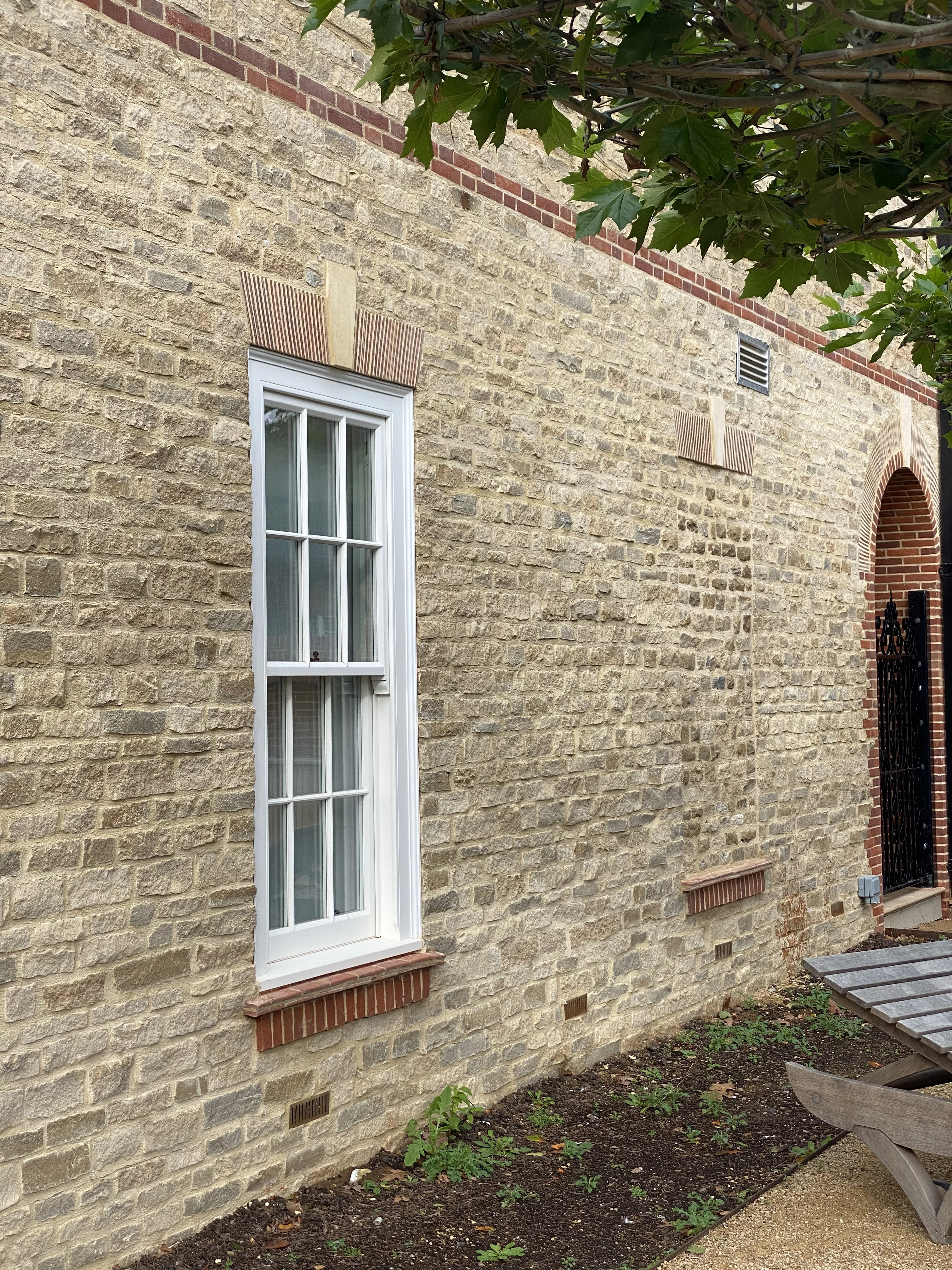 Natural stone walling with a tall white sash window and brick arches over the window
