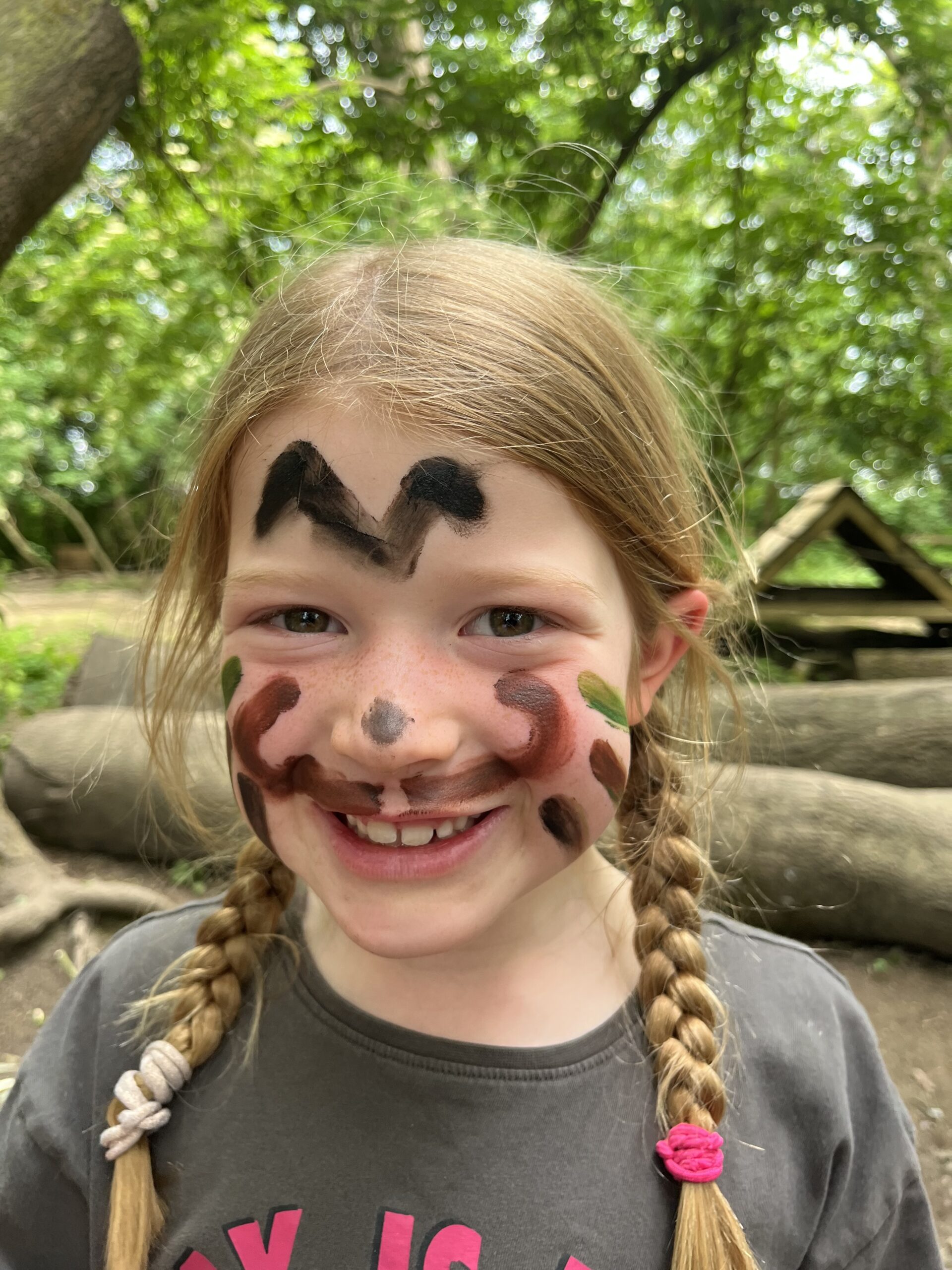 A young girl with face paint, smiling while playing outdoors on a school trip.