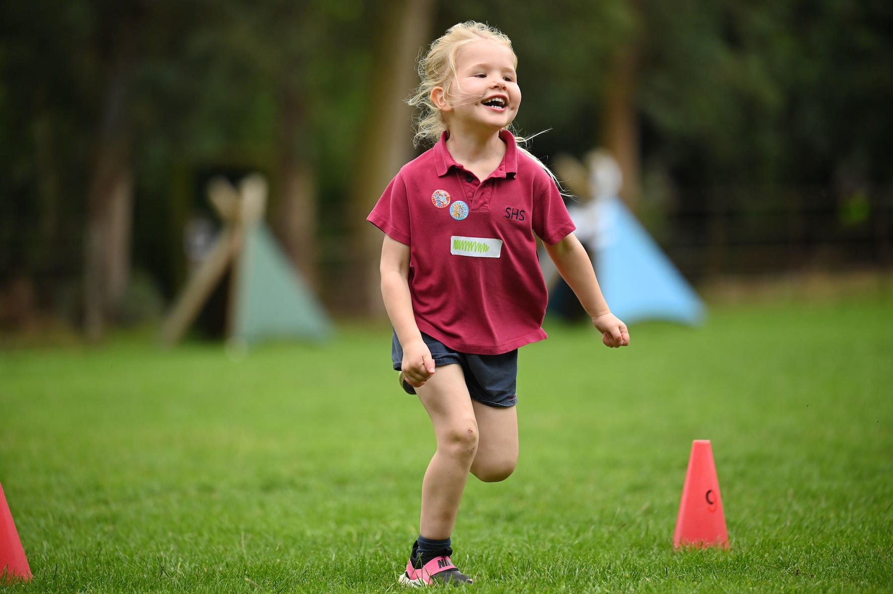Reception-aged child smiling and running outdoors at Swanbourne House school near Milton Keynes.